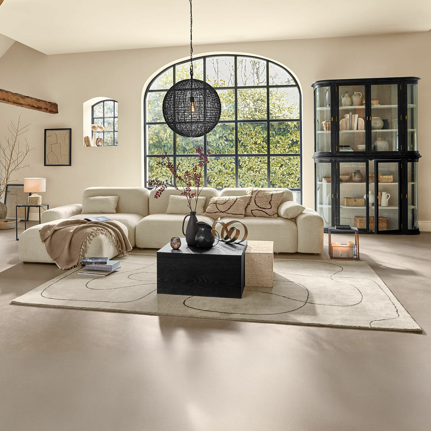 Tappeto Lavinois Ampio soggiorno con divano beige in tessuto, tavolino nero in legno e grande finestra con vista sul verde