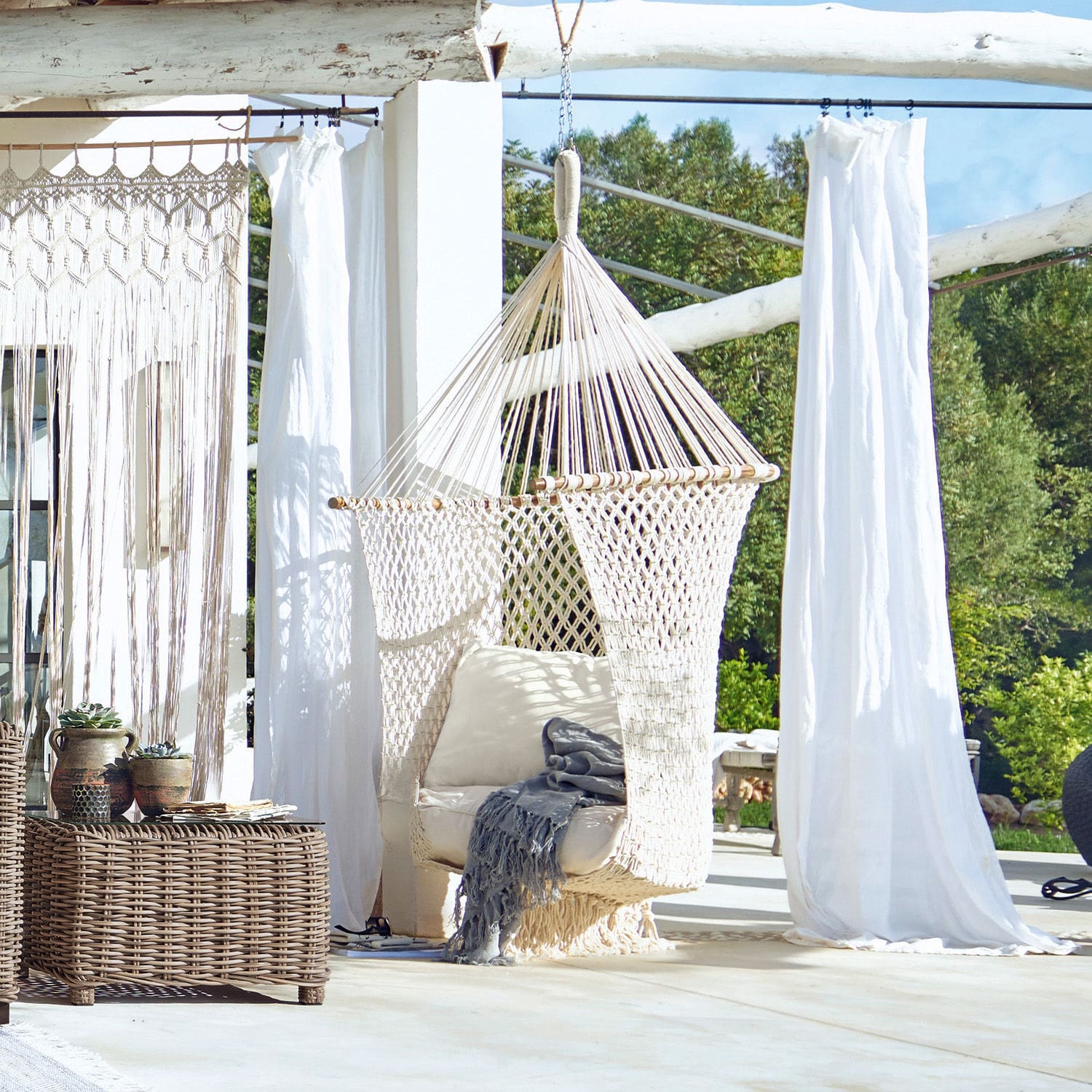 Poltrona sospesa Raffaelle Sedia sospesa in corda di cotone intrecciata color crema con cuscino su terrazza soleggiata