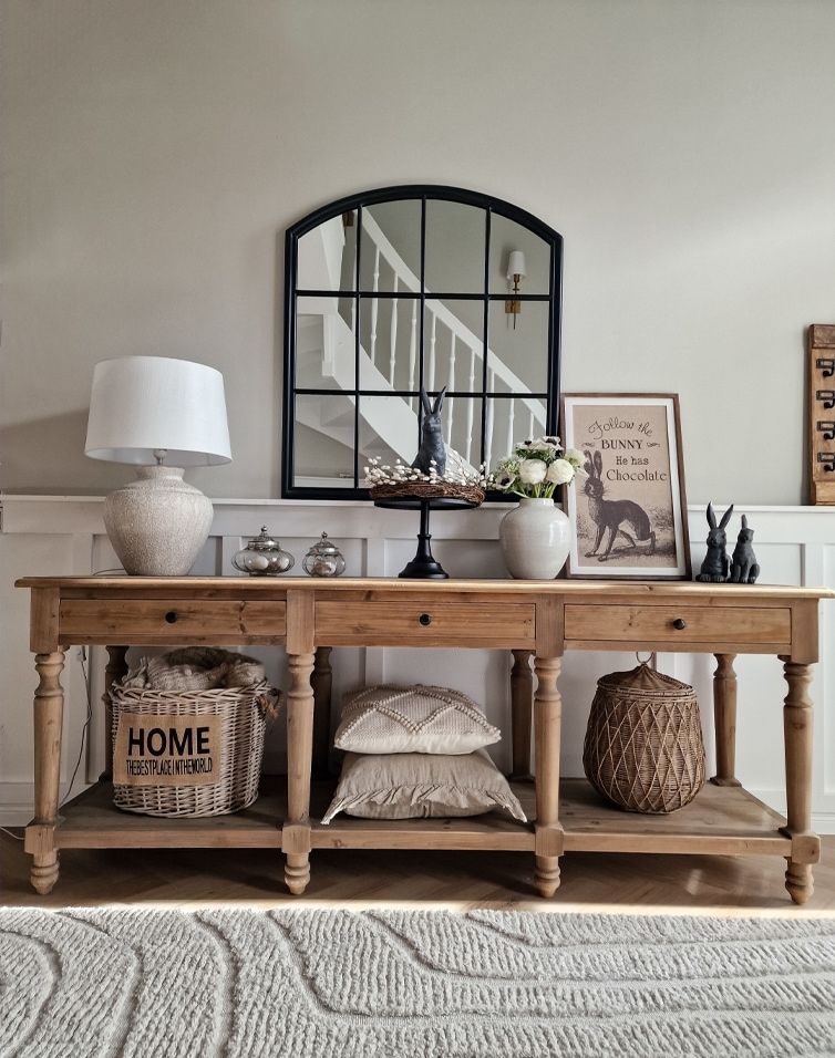 Tavolo in legno con decorazioni rustiche, specchio con cornice nera e lampada da tavolo in ambiente accogliente