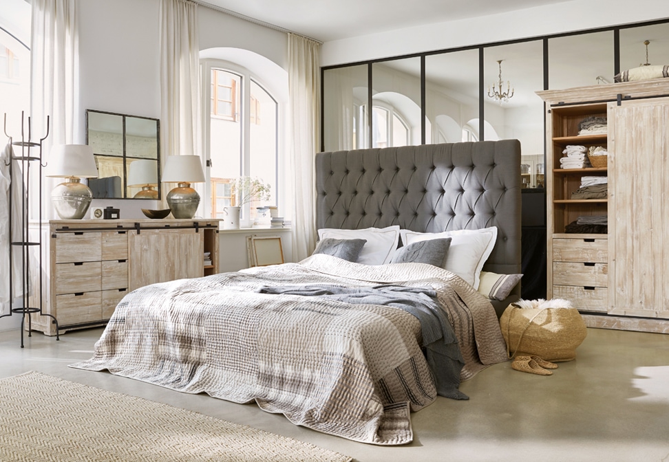 Camera da letto accogliente con testiera imbottita grigia e mobili in legno chiaro stile loft