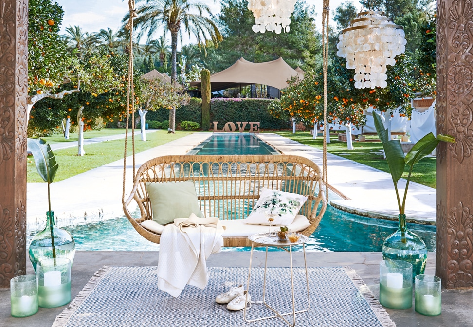 Altalena in rattan con cuscini sopra piscina in giardino con alberi di arancio e decorazioni