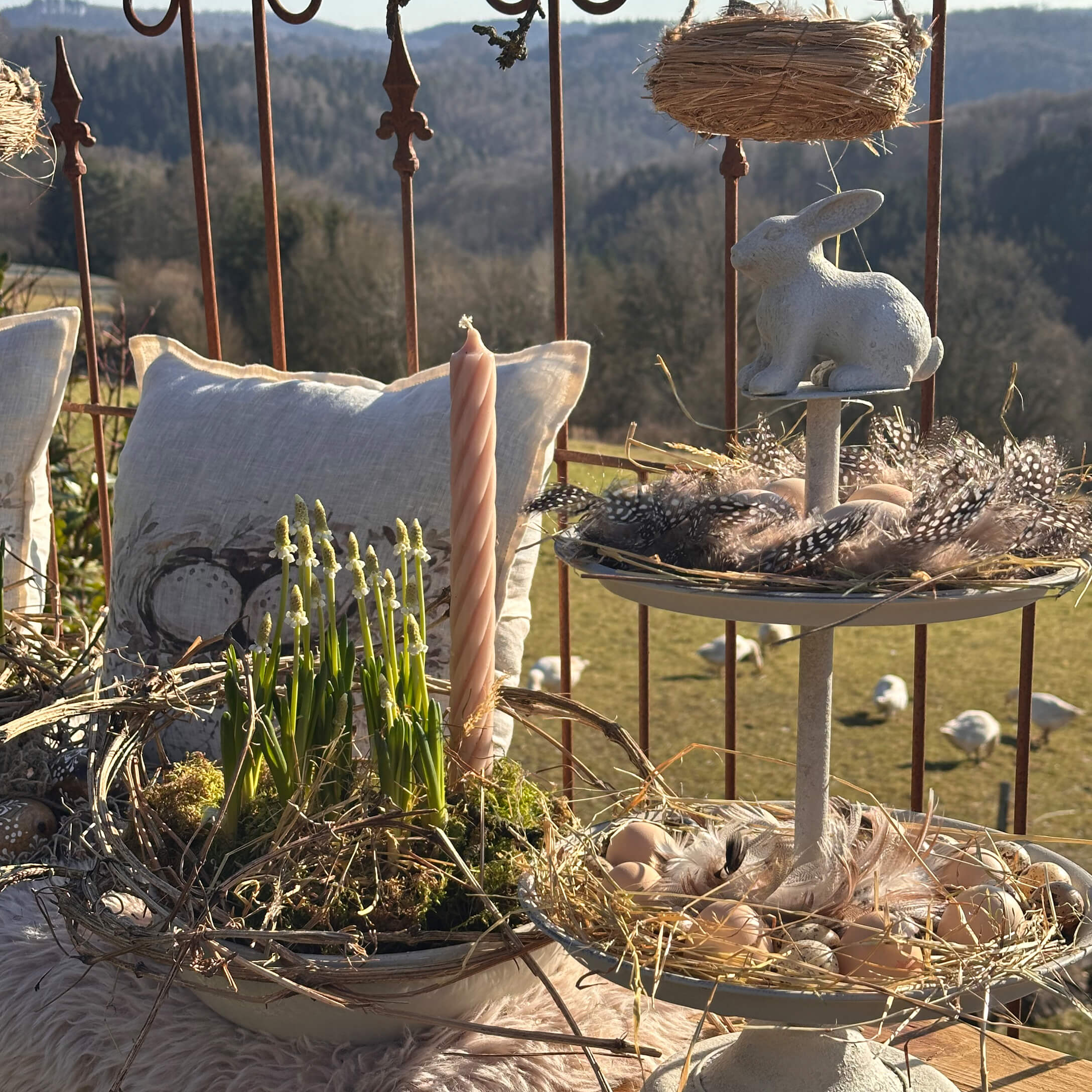 Decorazione pasquale naturale con coniglio bianco, piume e candela su sfondo rustico con cuscini