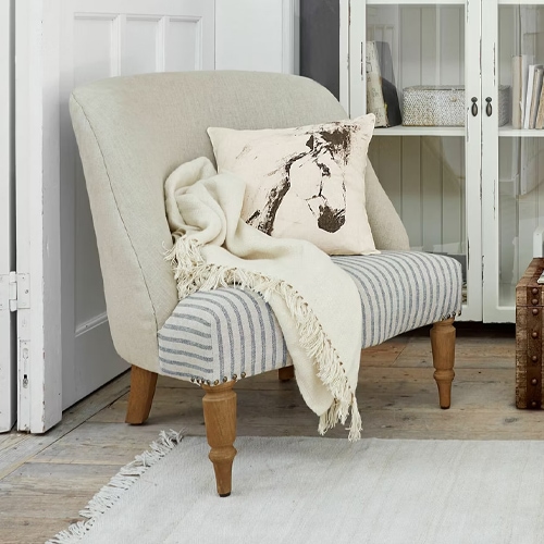 Divano bicolore in tessuto a righe con schienale beige e gambe in legno, decorato con cuscino e coperta