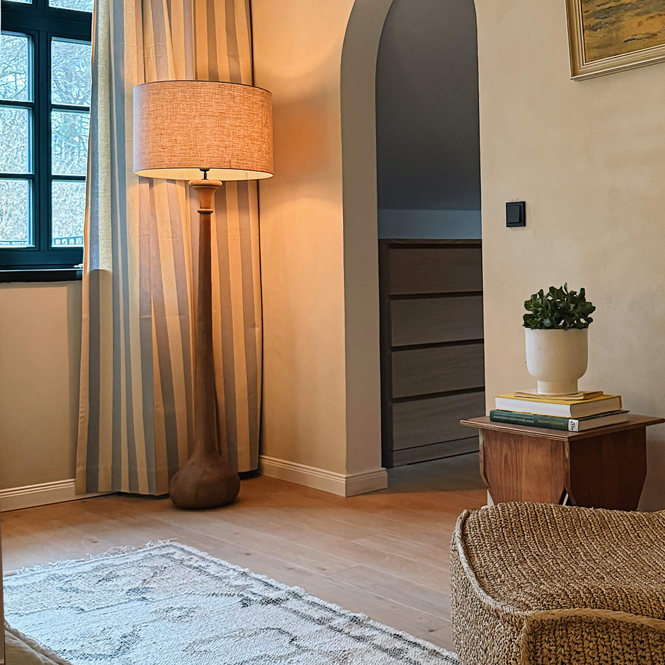 Lampada da terra in legno con paralume beige in soggiorno accogliente con tappeto naturale e pianta