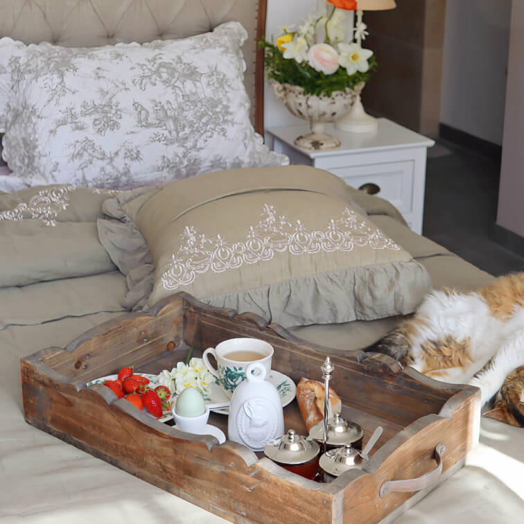Vassoio in legno sul letto con tazza di tè, uovo e fragole, camera accogliente con cuscini ricamati