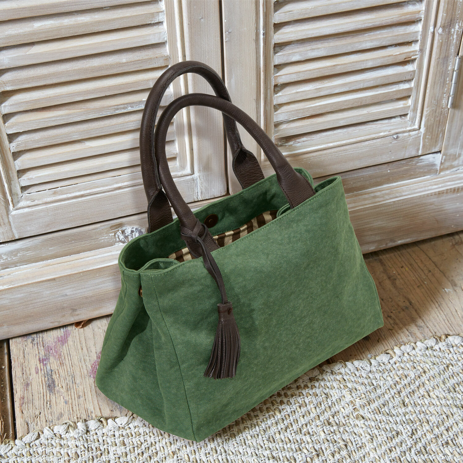 Borsa Hoya Borsa verde in tessuto con manici in pelle marrone e nappina su pavimento in legno chiaro