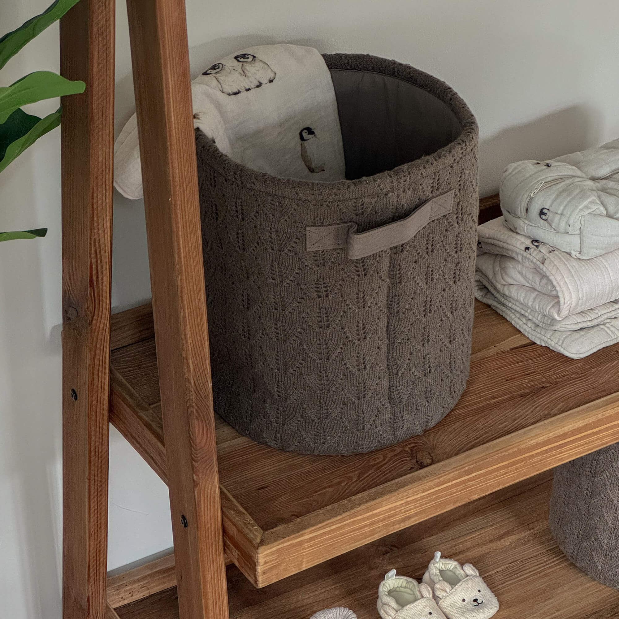Cesto intrecciato marrone su mensola in legno con tessuto morbido e scarpine per bambini beige