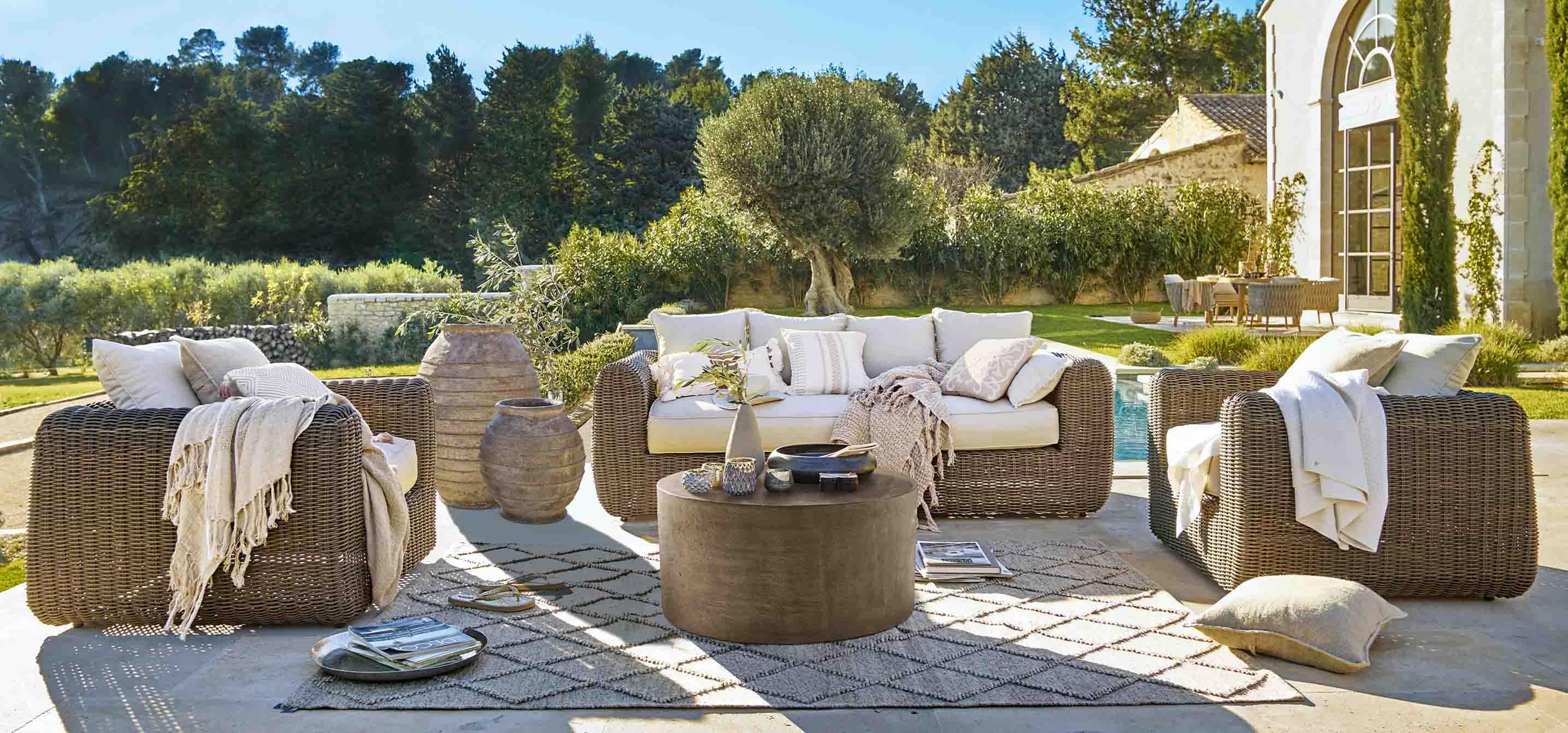 Set di mobili da giardino in rattan marrone con cuscini crema e tavolino rotondo su terrazza soleggiata