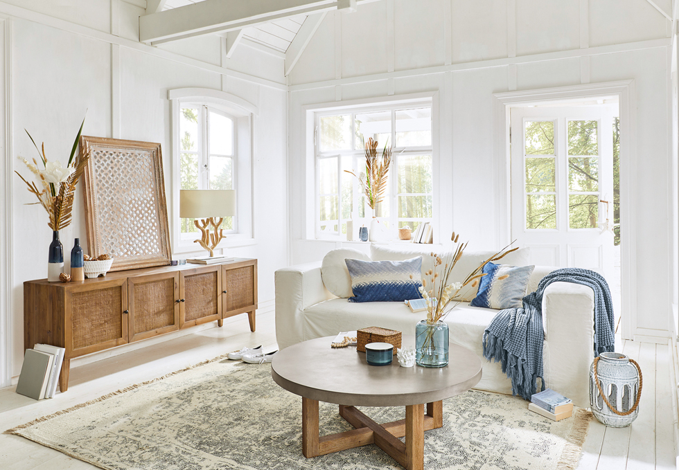 Soggiorno luminoso in stile marinaro con divano bianco, credenza in legno e dettagli blu