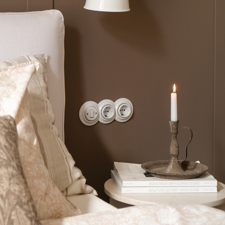 Portacandele in metallo rustico con candela bianca su tavolino accanto a letto con biancheria beige