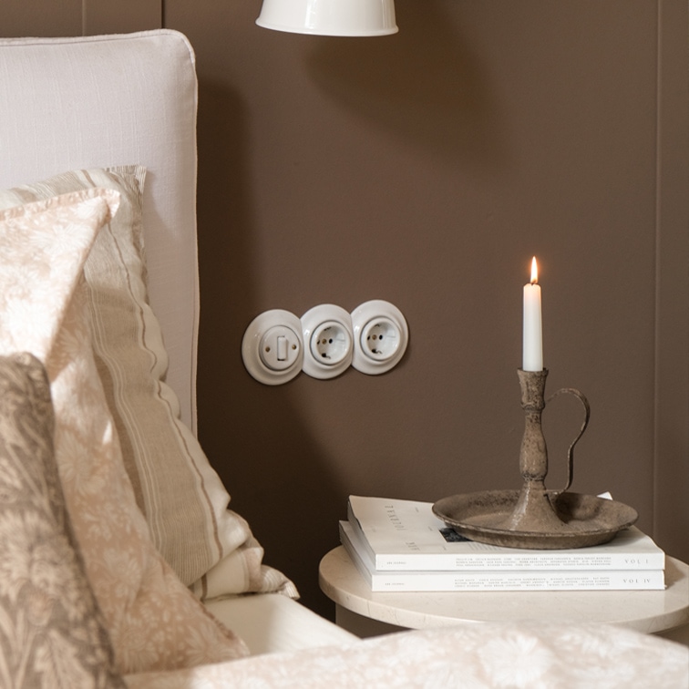 Portacandele in metallo rustico con candela bianca su tavolino accanto a letto con biancheria beige