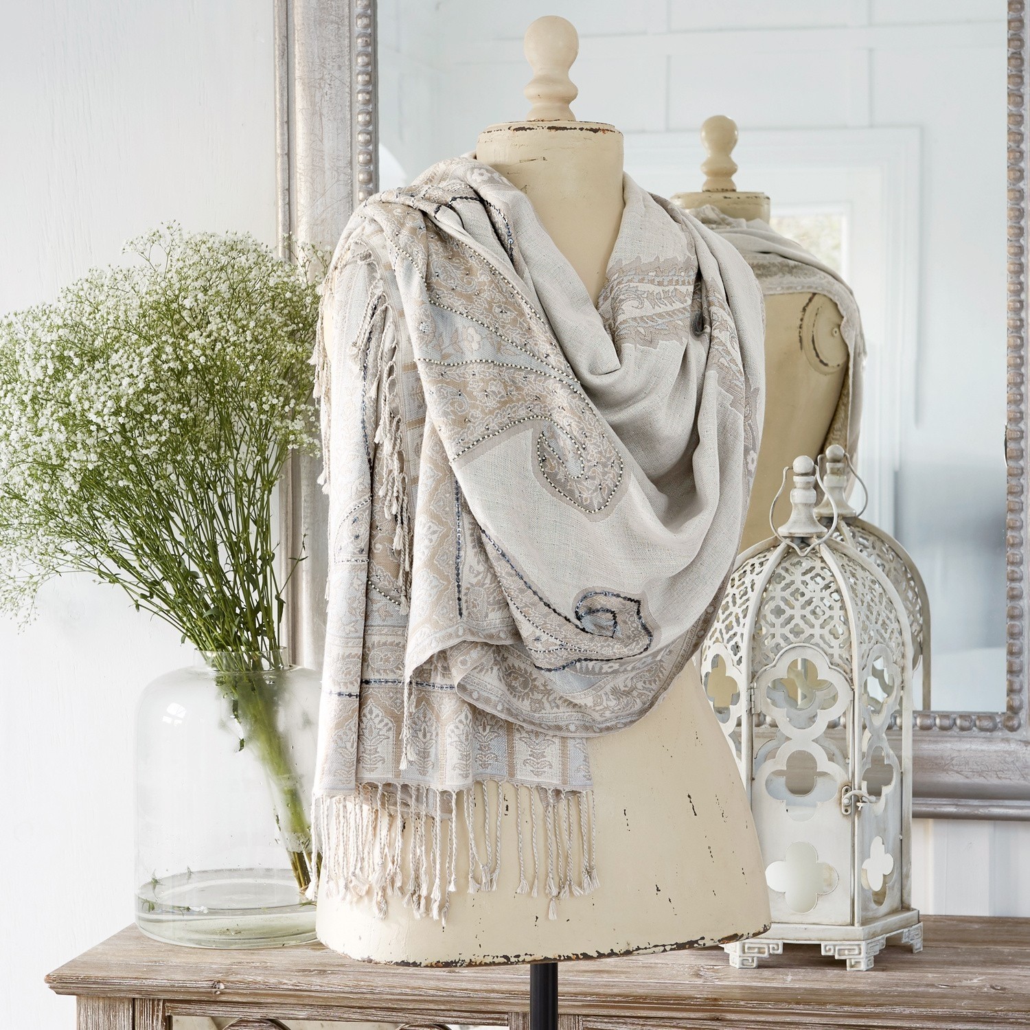 Scialle Moyra Sciarpa beige con motivo paisley e frange su manichino, decorazione d'interni con lanterna e fiori