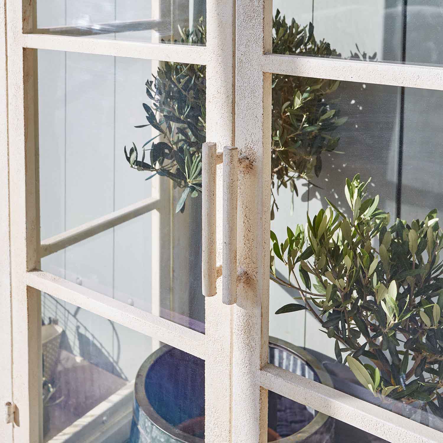 Porta in metallo bianco con maniglie e piante verdi sullo sfondo, decorazione da giardino