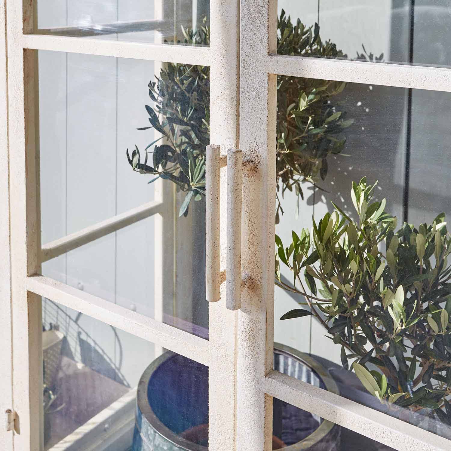 Porta in metallo bianco con maniglie e piante verdi sullo sfondo, decorazione da giardino