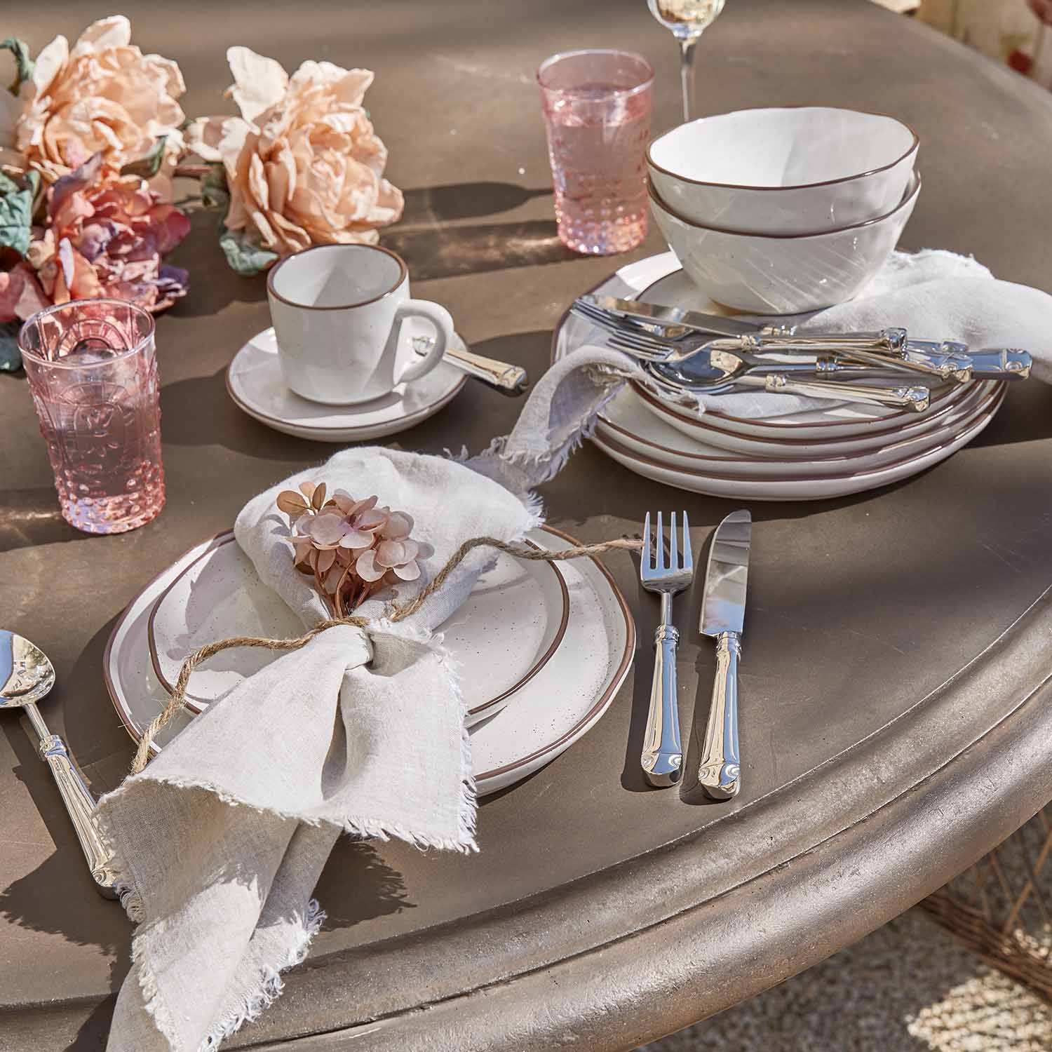 Servizio di ceramica bianca con bordo marrone, bicchieri rosa e posate su tavolo