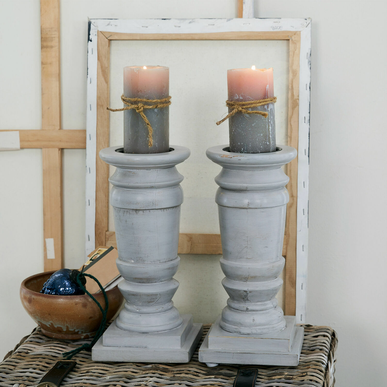 Coppia di candelieri Lobata Coppia di portacandele in legno grigio con candele grigie e decorazioni in corda su tavolo in vimini