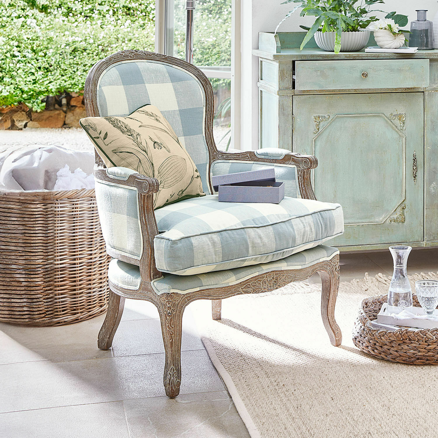 Poltrona Quintelais Poltrona in legno con tessuto a quadri blu e beige, cuscino decorativo con motivo vegetale in ambiente luminoso