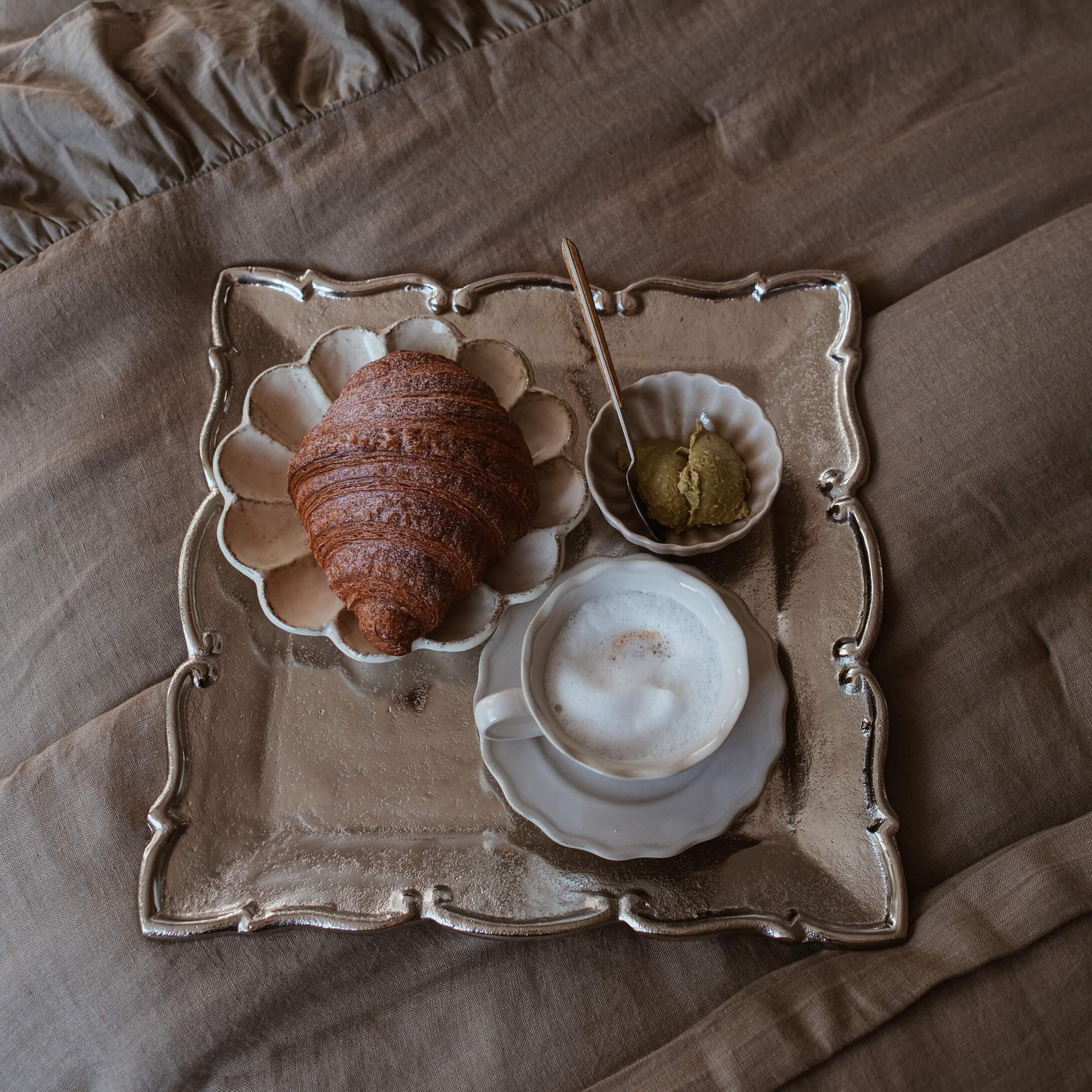 Vassoio con croissant, caffè con schiuma e crema su tessuto beige, stile slow living