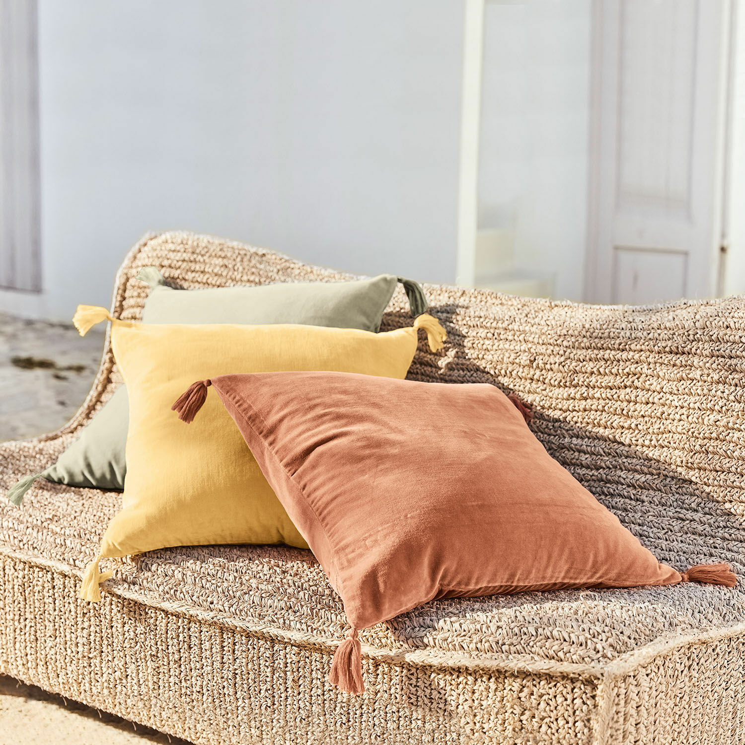 Set di 3 copricuscini Bedir Tre cuscini decorativi in cotone terracotta, giallo e verde su seduta intrecciata all'aperto