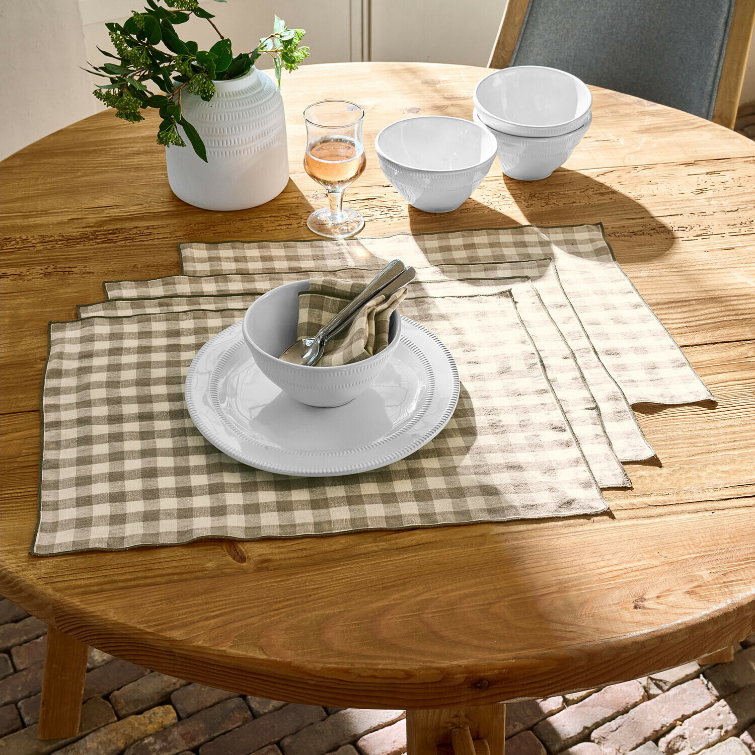 Ciotole e piatto in ceramica bianca su tavolo in legno con tovagliette in lino beige a quadri