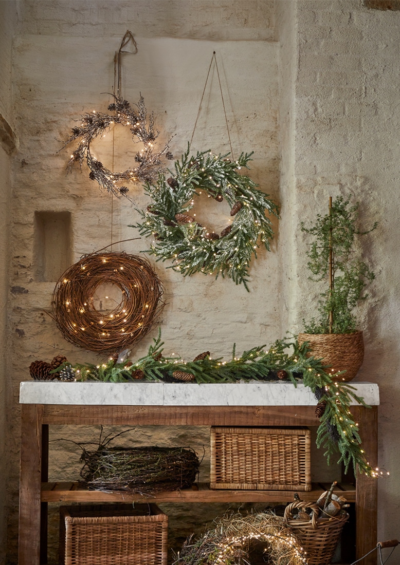 Ghirlande natalizie decorative di rami e luci appese a muro in pietra e tavolo in legno con marmo