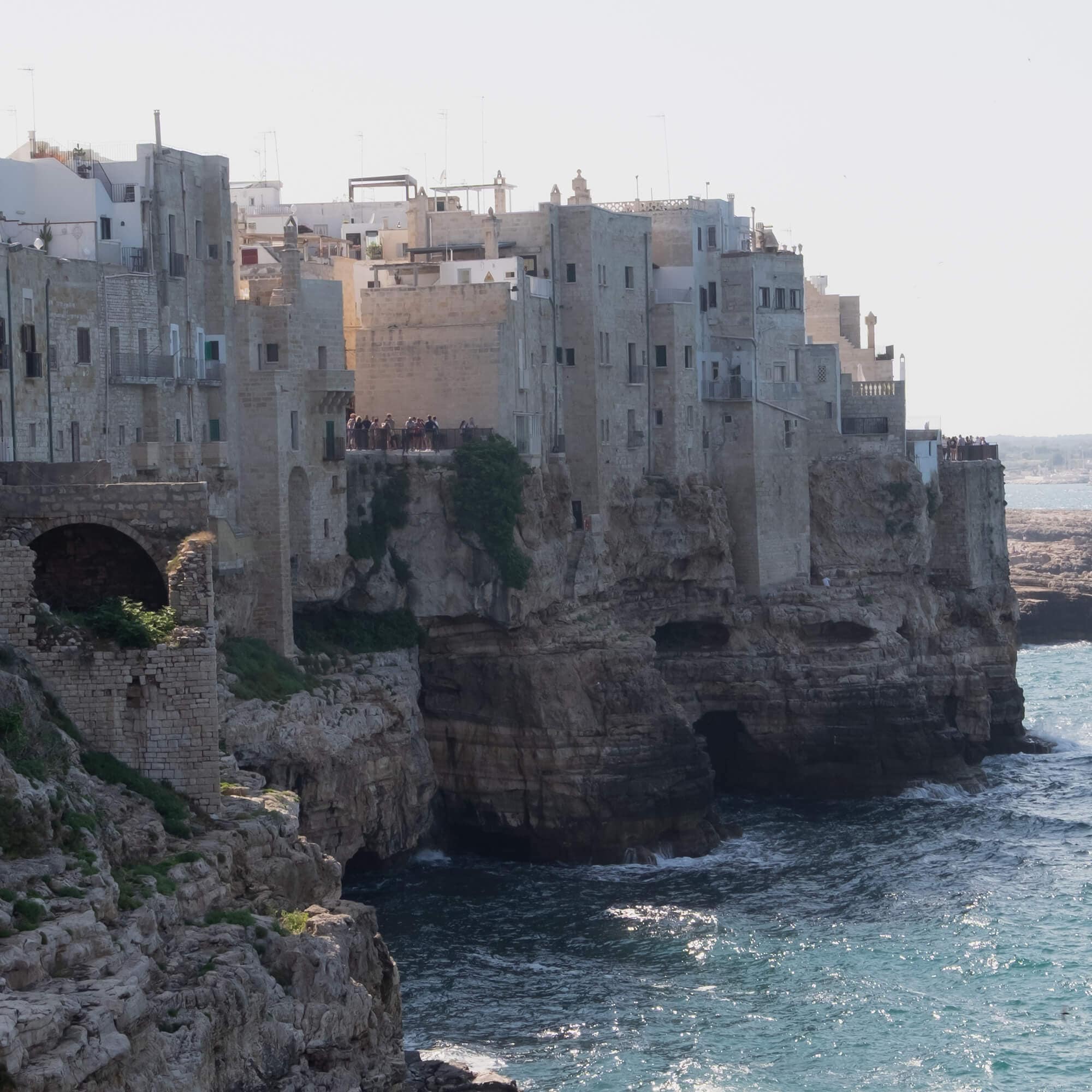 Vecchi edifici in pietra su una scogliera sopra il mare con acqua turchese e rocce sottostanti