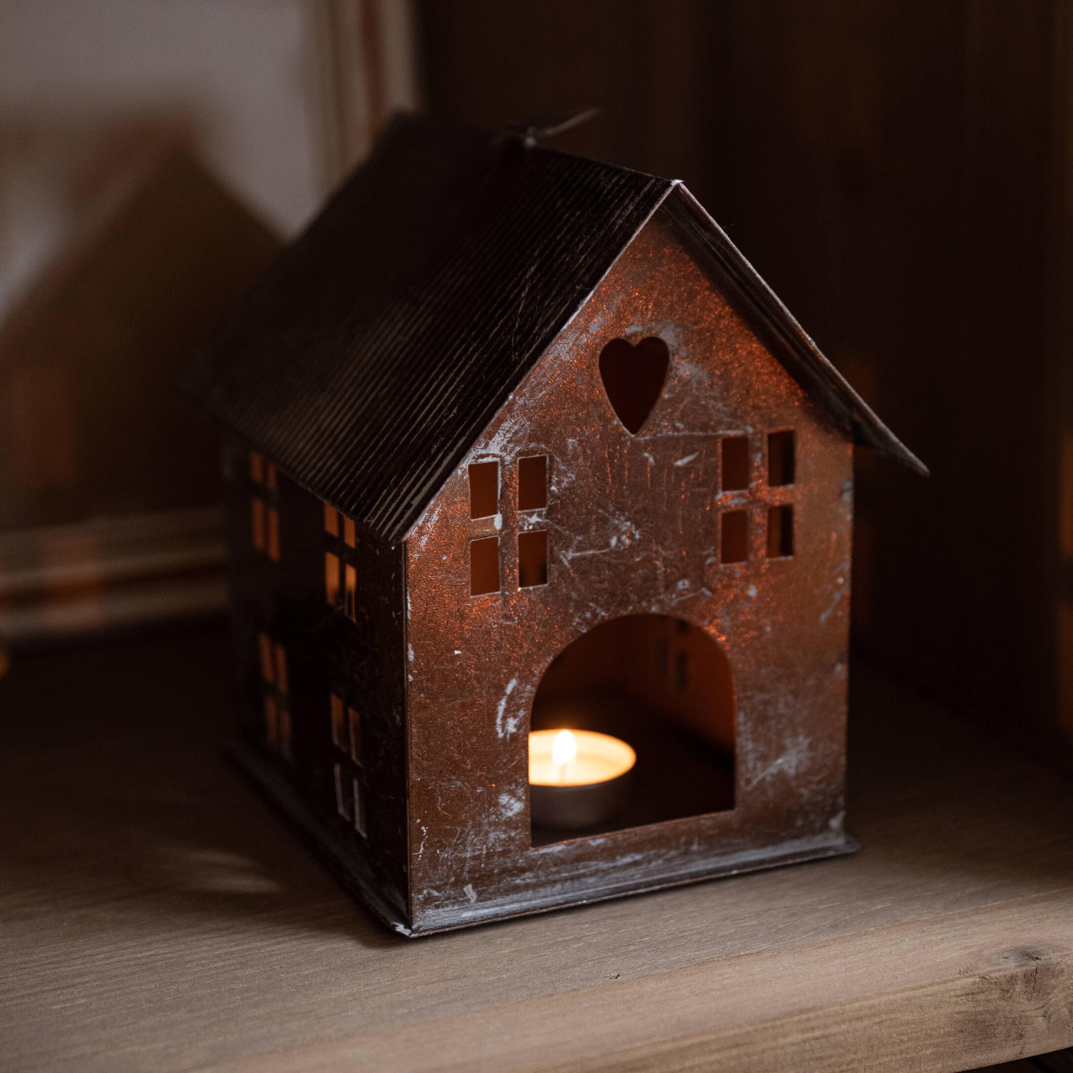 Lanterna in metallo a forma di casa con cuore ritagliato e candela accesa su mensola di legno