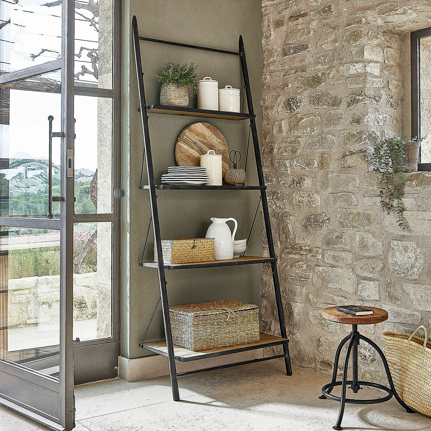 Scaffale Greenbriar Scala nera in metallo con ripiani in legno e decorazioni in interno rustico con muro in pietra