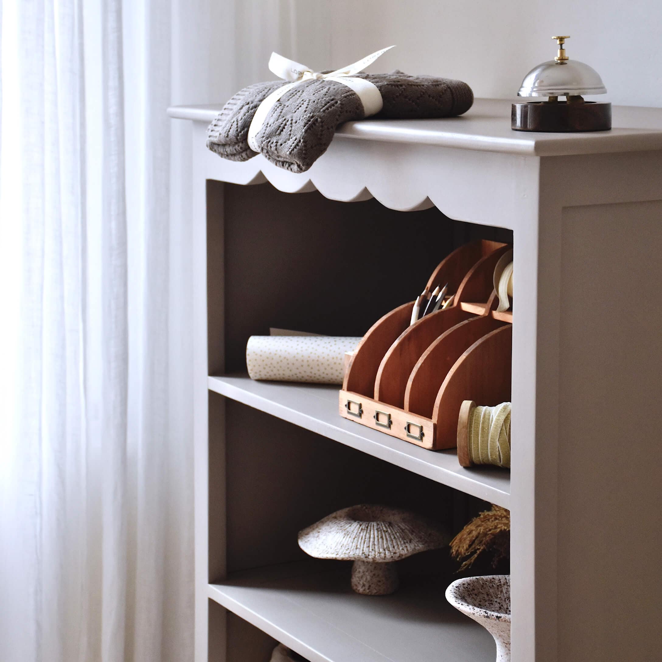 Scaffale in legno grigio con oggetti decorativi e tessuto lavorato a maglia grigio sopra