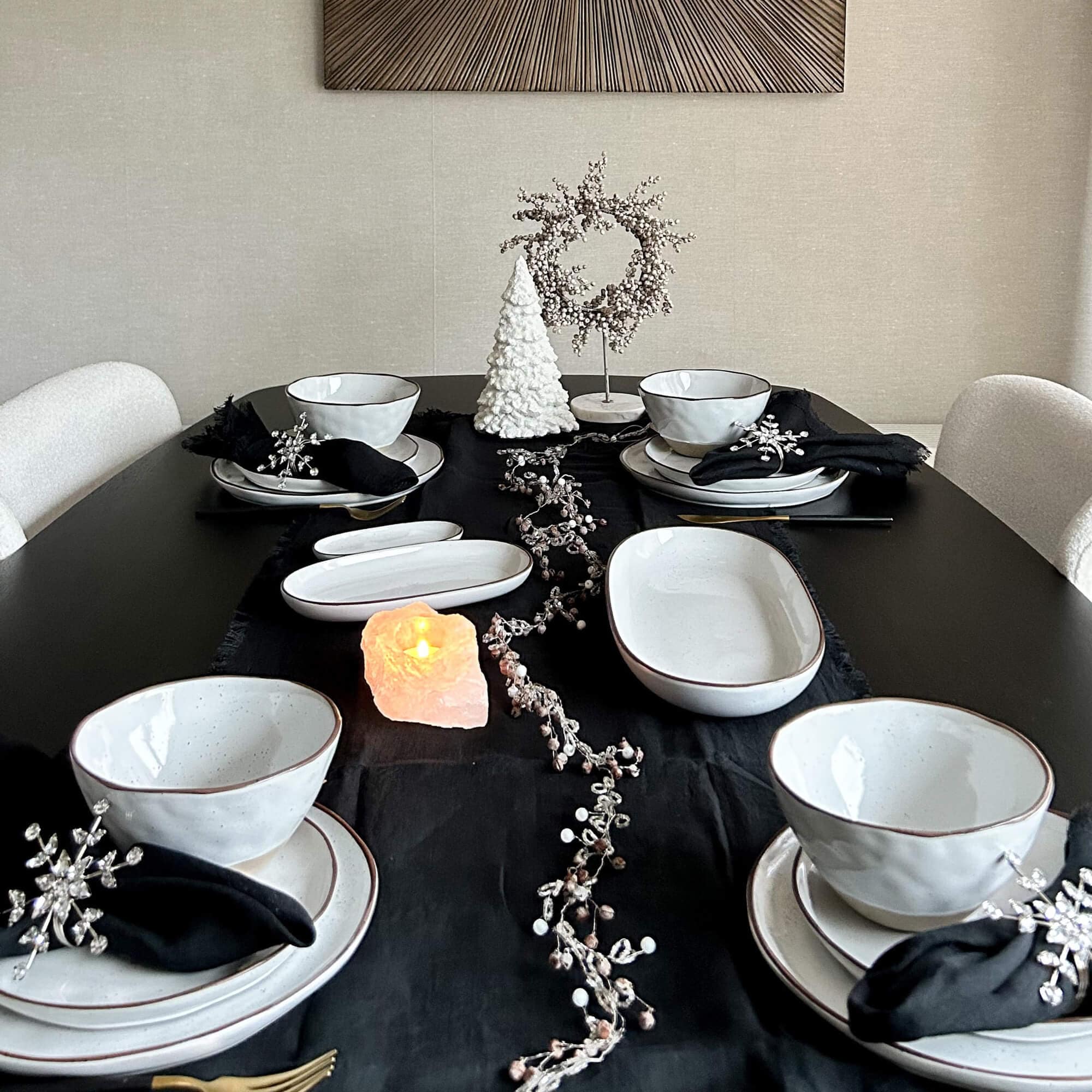 Servizio di piatti in ceramica bianca su tovaglia nera con decorazioni natalizie e candela di sale