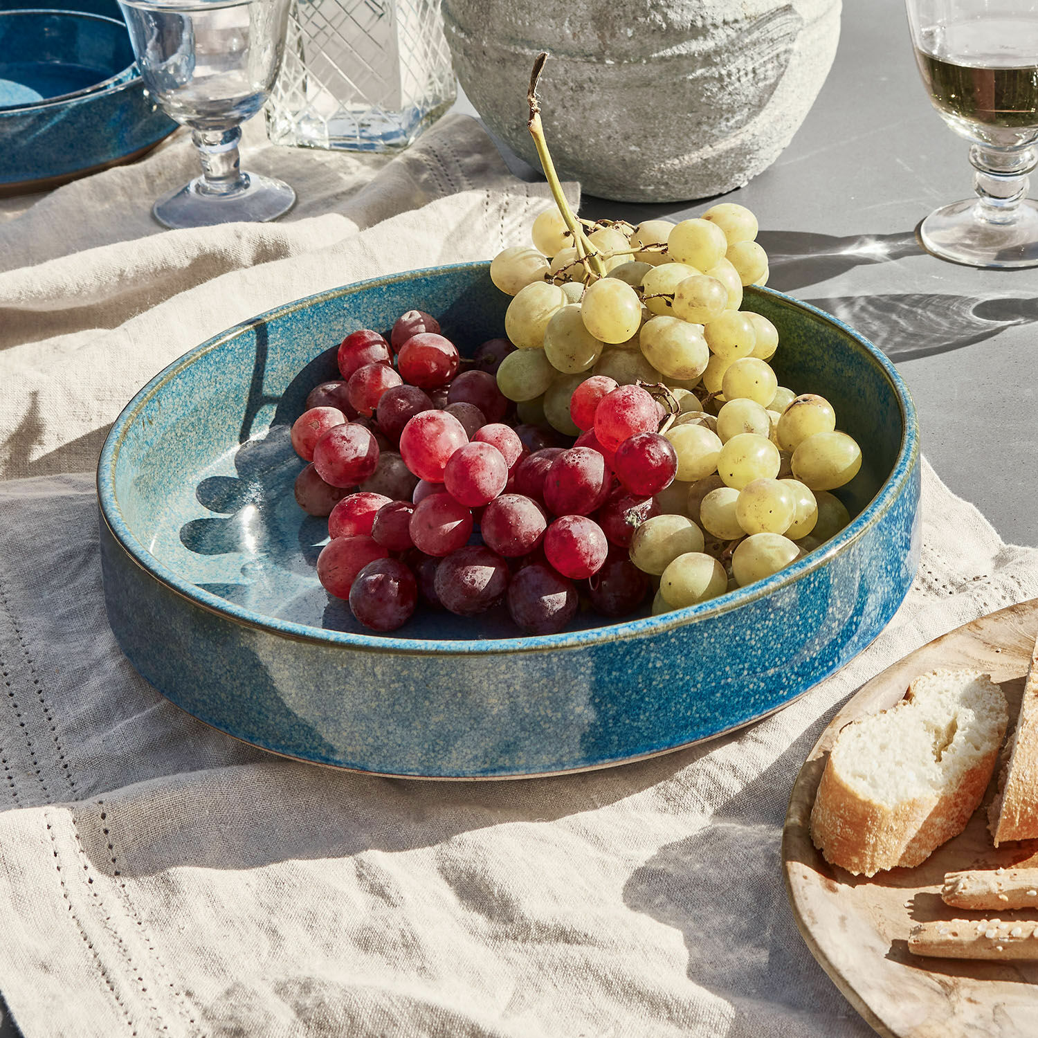 Insalatiera Darney Grande ciotola in ceramica blu con uva rossa e verde su tovaglia di lino, decorazione tavola