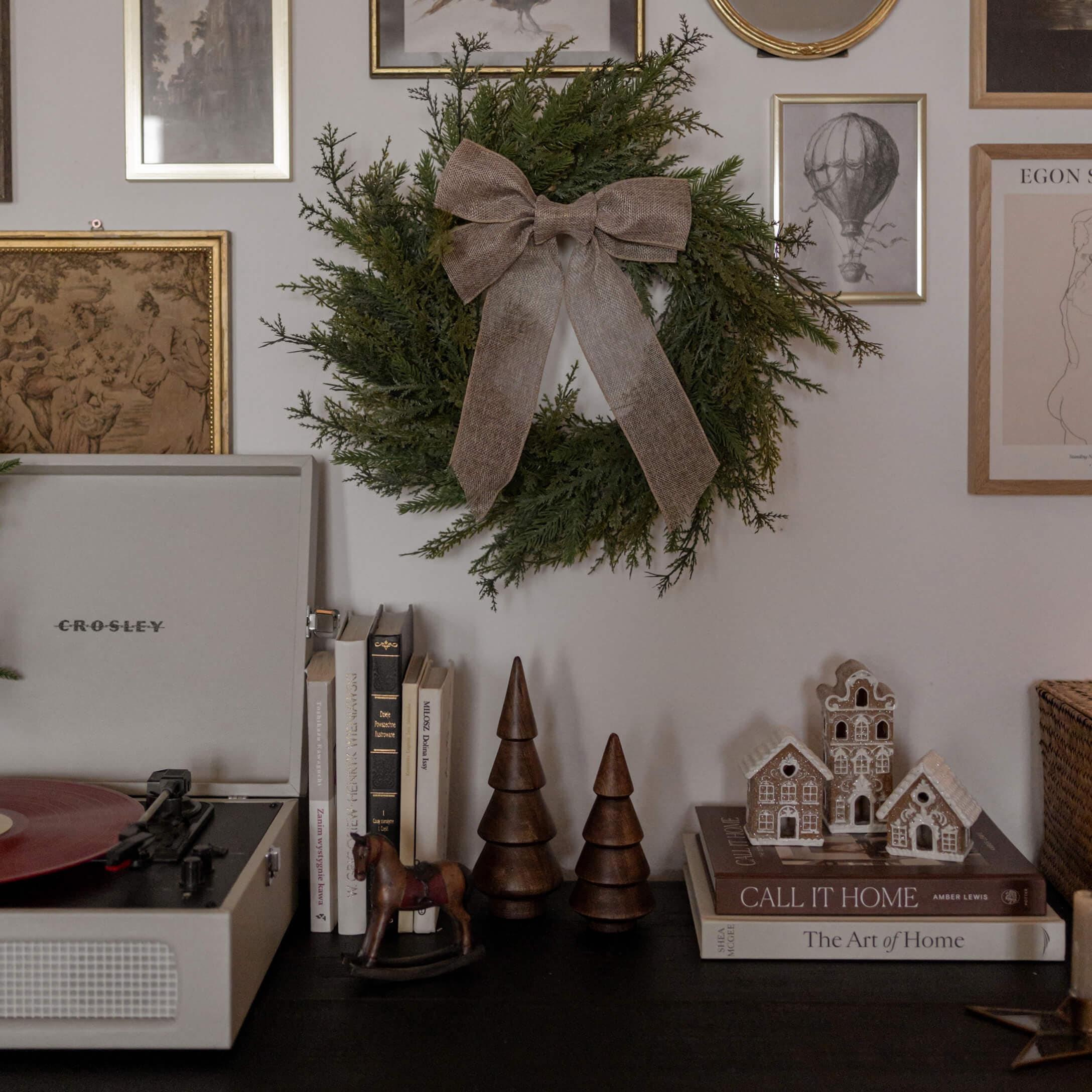 Corona decorativa verde con fiocco marrone appesa al muro sopra tavolo nero con libri e decorazioni