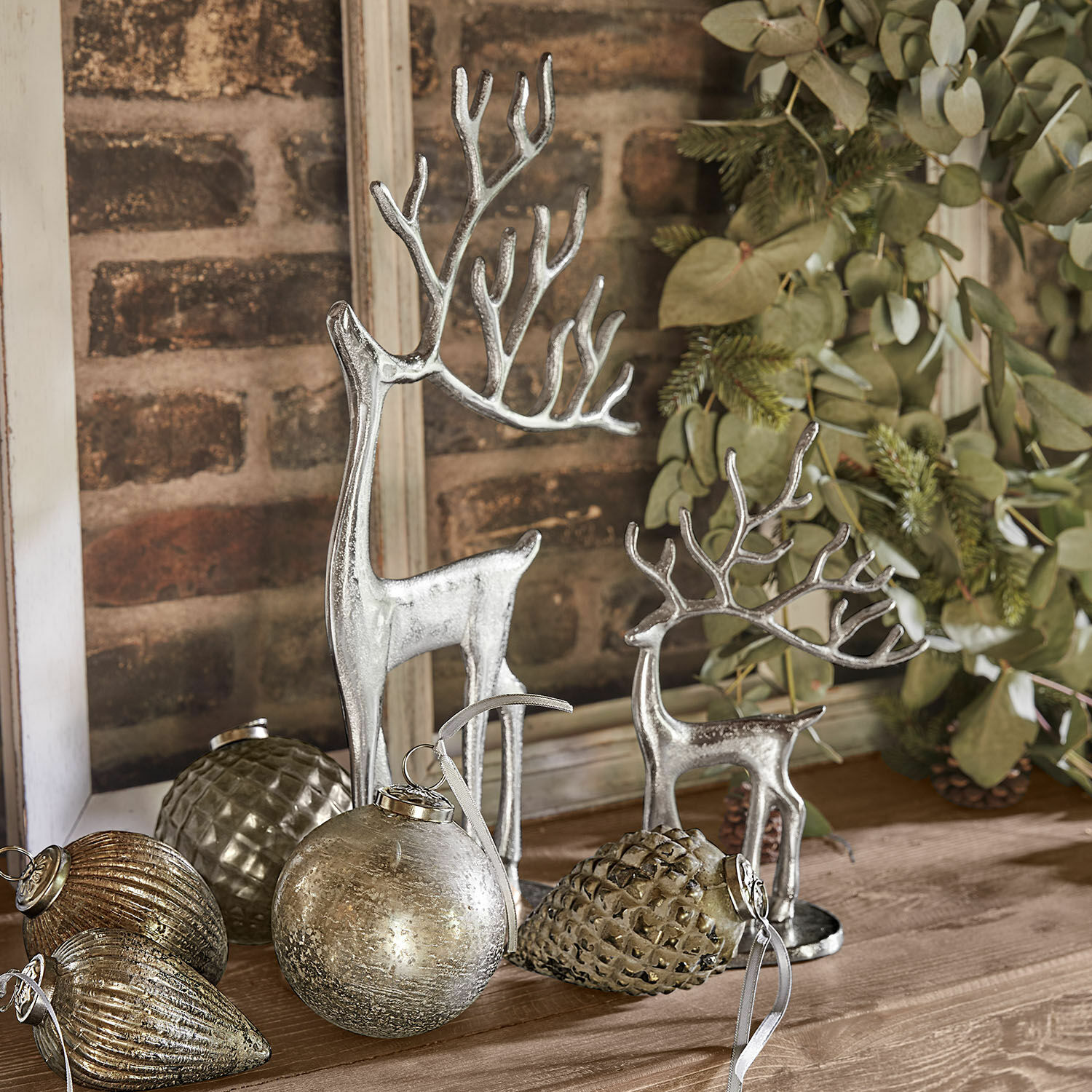 Set di 2 renne decorative Zerlay Figure di renne argentate e decorazioni natalizie su tavolo in legno con rami verdi sullo sfondo