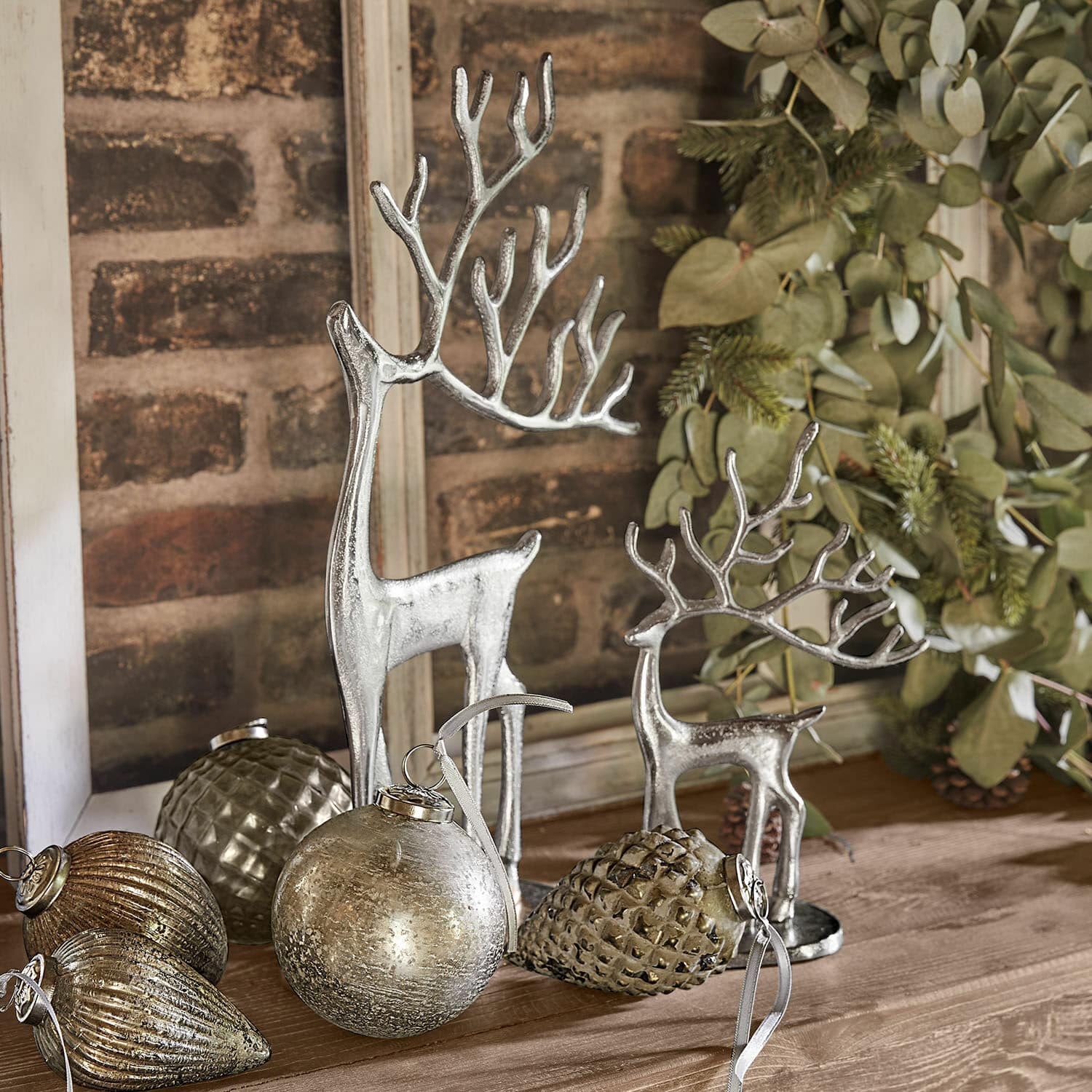Set di 2 renne decorative Zerlay Figure di renne argentate e decorazioni natalizie su tavolo in legno con rami verdi sullo sfondo