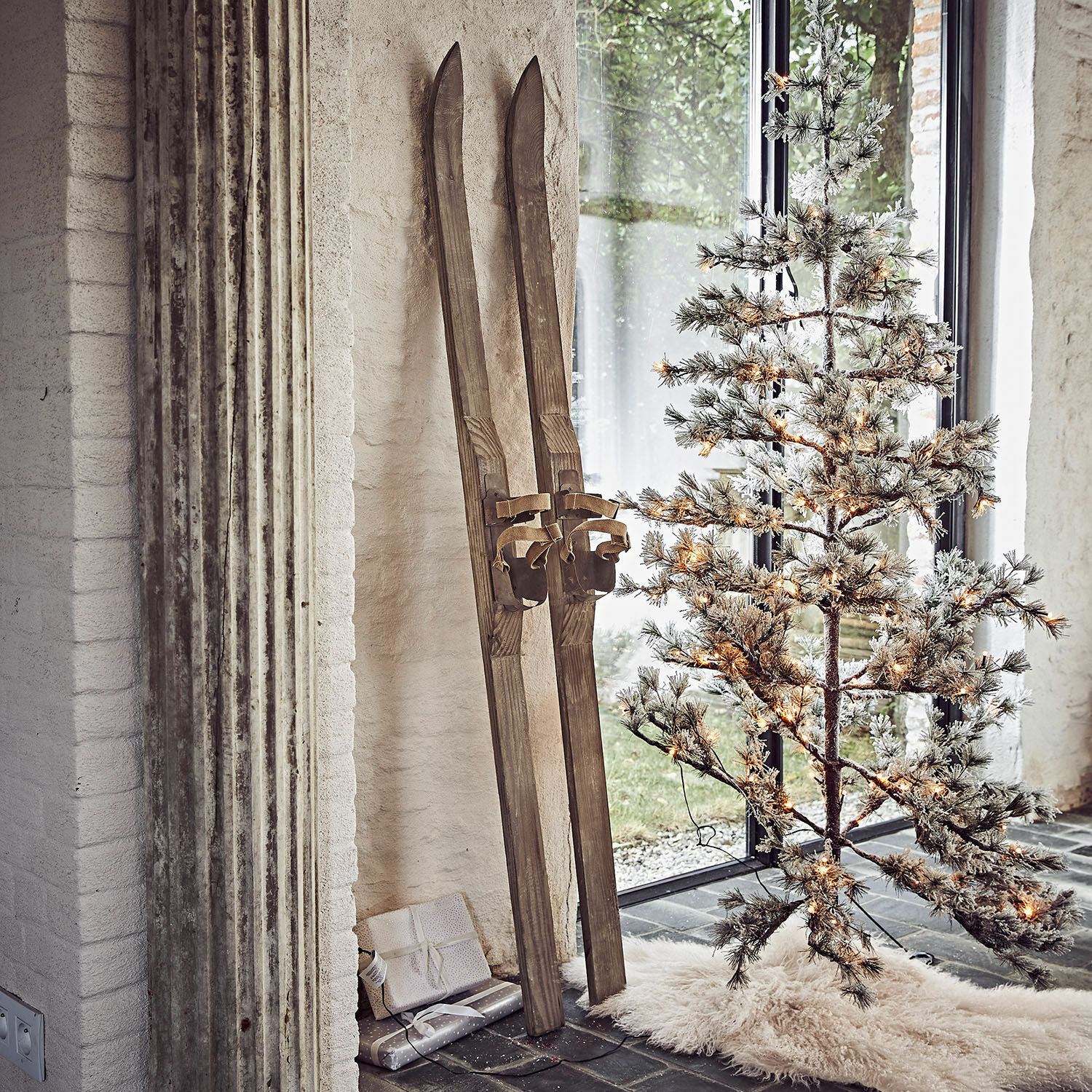 Coppia di sci decorativi Lambeth Sci in legno vintage accanto ad albero di Natale artificiale illuminato su tappeto bianco