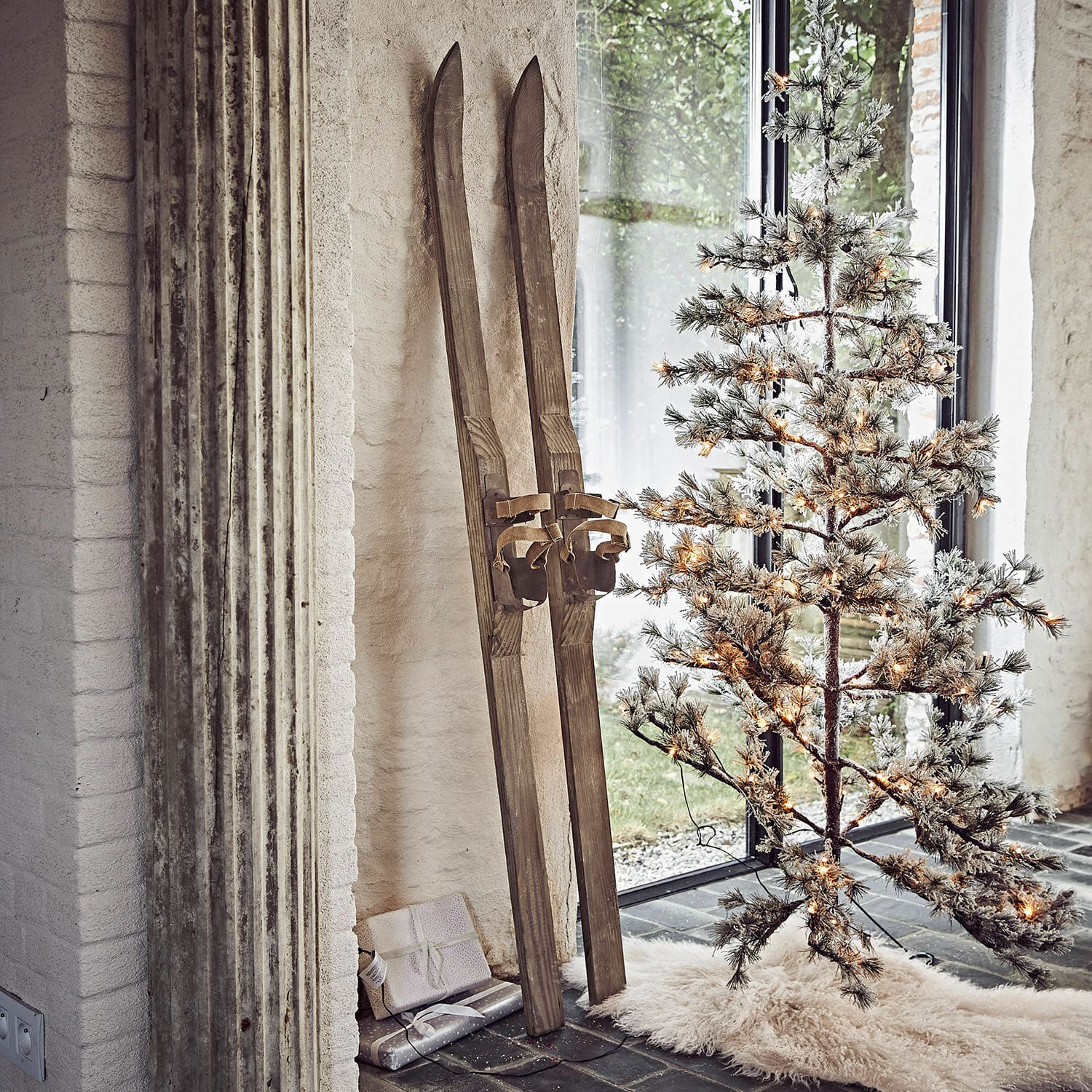 Coppia di sci decorativi Lambeth Sci in legno vintage accanto ad albero di Natale artificiale illuminato su tappeto bianco