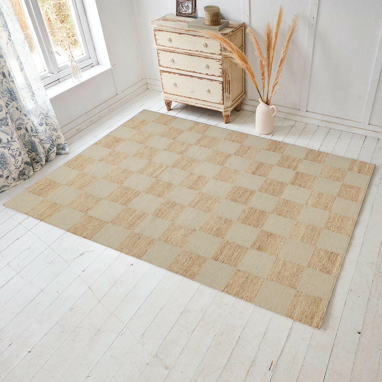 Tappeto Nexari Tappeto beige a quadri in materiale naturale su pavimento in legno chiaro in stanza luminosa