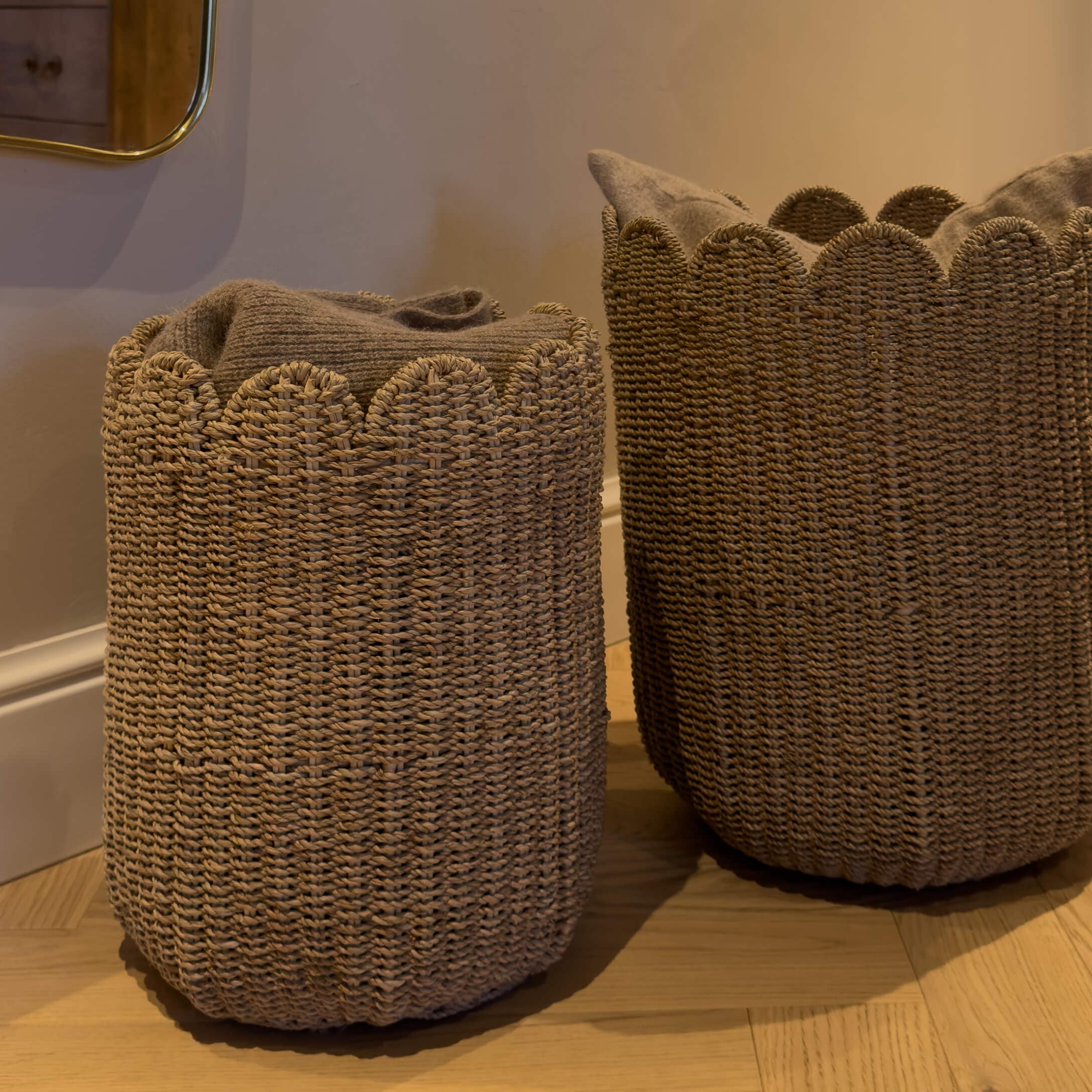 Due ceste intrecciate marroni con bordo ondulato, piene di coperte morbide su pavimento in legno