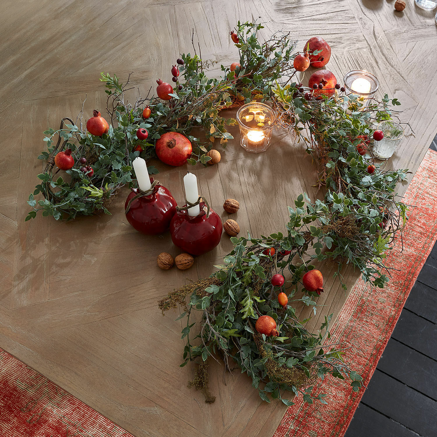 Festone Karidah Corona decorativa con foglie verdi e frutti rossi su tavolo in legno con candele accese