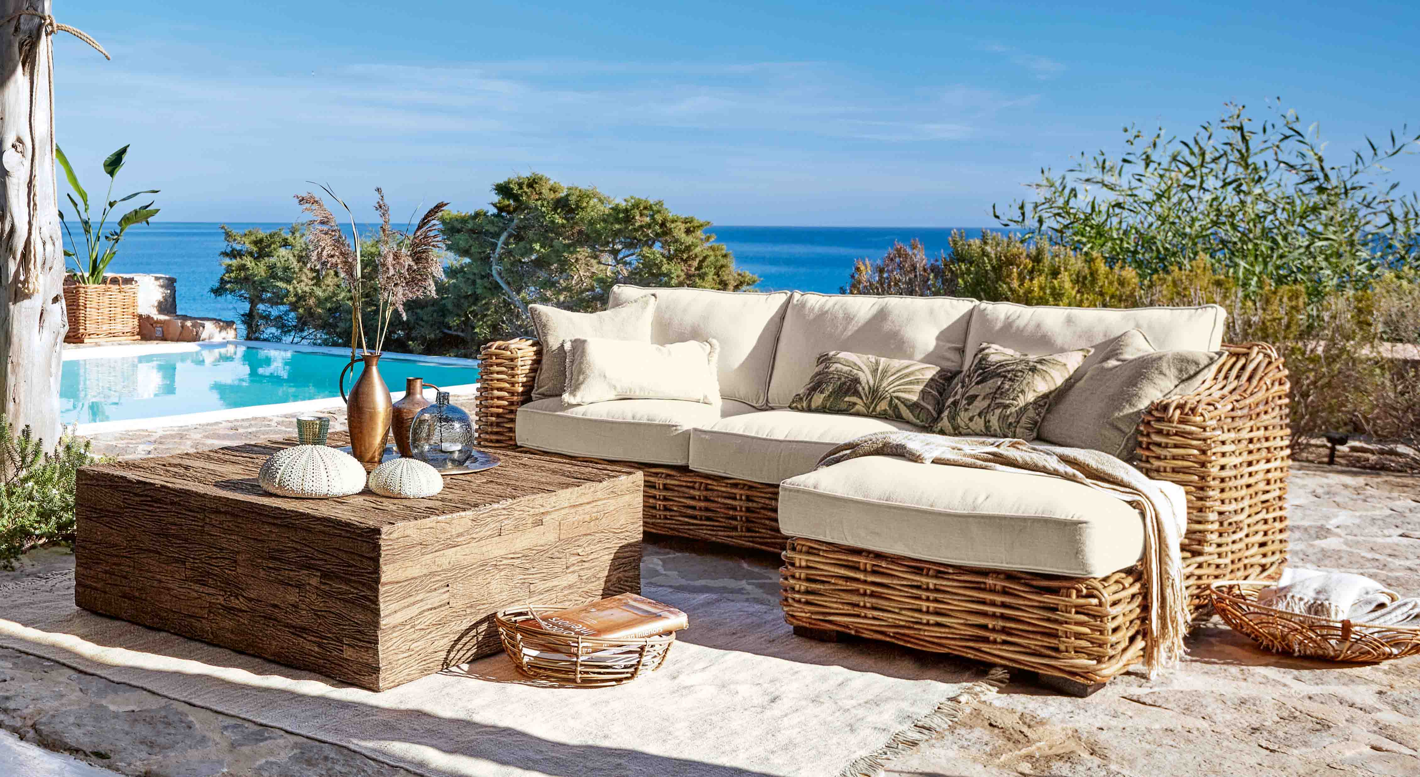 Set di mobili da giardino in rattan con cuscini crema vicino a piscina con vista mare
