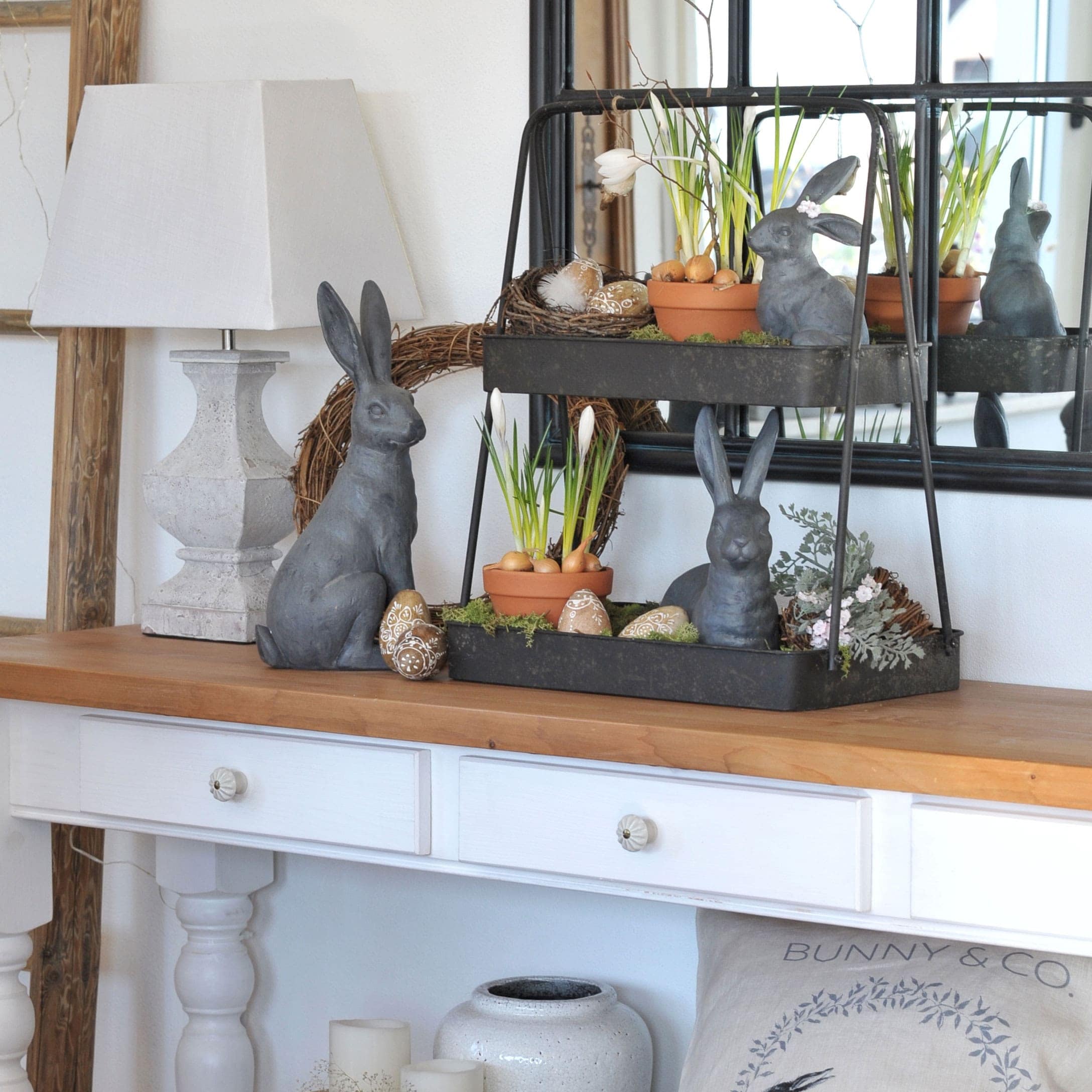 Decorazione pasquale con conigli grigi, vasi di fiori e uova decorative su tavolo in legno