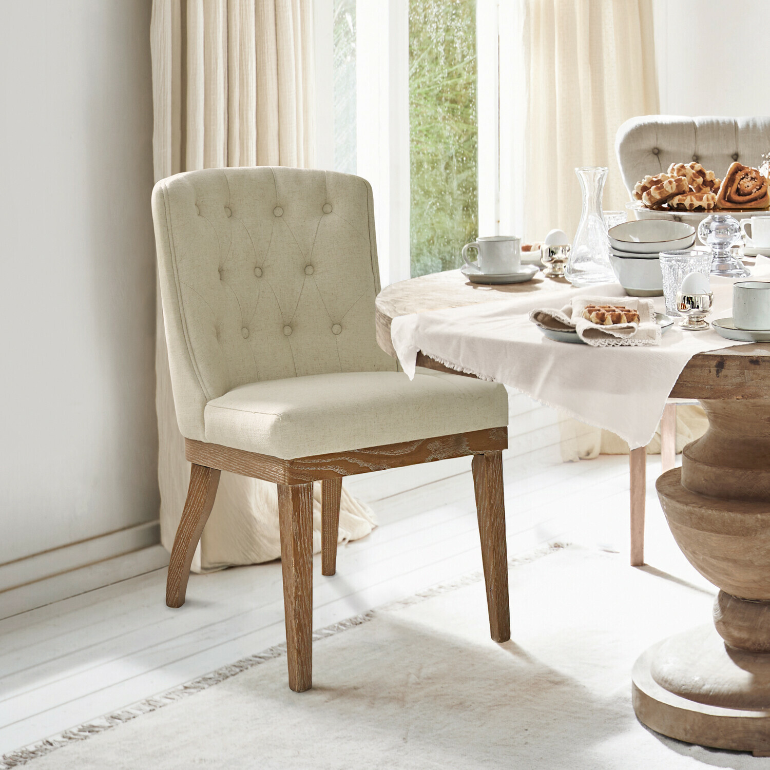 Sedia Fairwyn Sedia imbottita beige con gambe in legno accanto a tavolo da pranzo con stoviglie e dolci