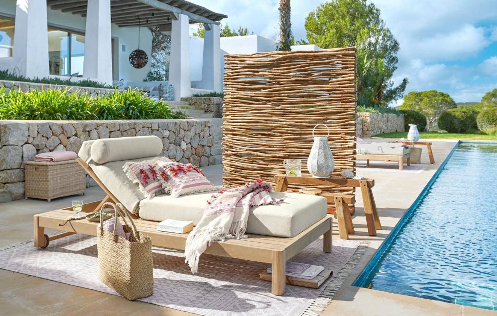 Lettino in legno chiaro con cuscino crema e paravento decorativo vicino alla piscina in stile marittimo