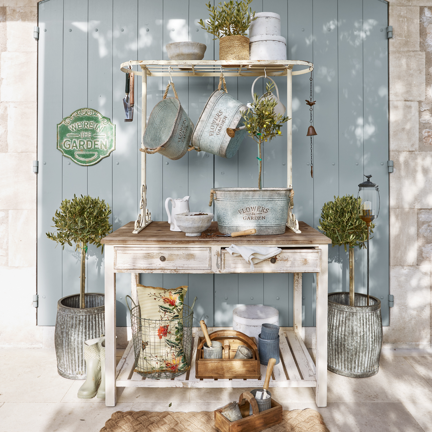 Tavolo da giardino bianco in legno con vasi in metallo e attrezzi da giardino davanti a porta blu