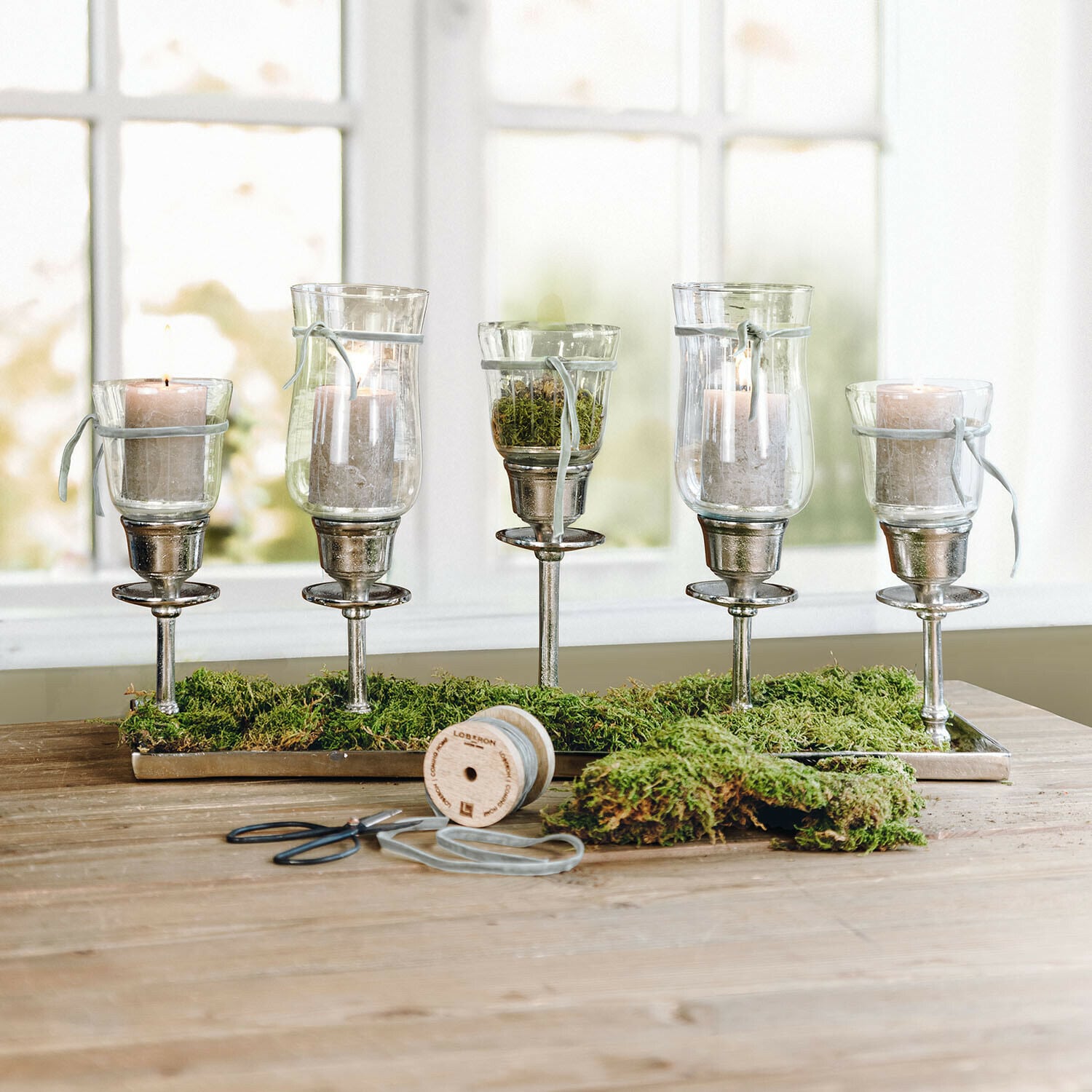 Set decorativo Buona Pasqua Osterfreude Set di cinque portacandele in vetro su supporti metallici con muschio verde su tavolo in legno