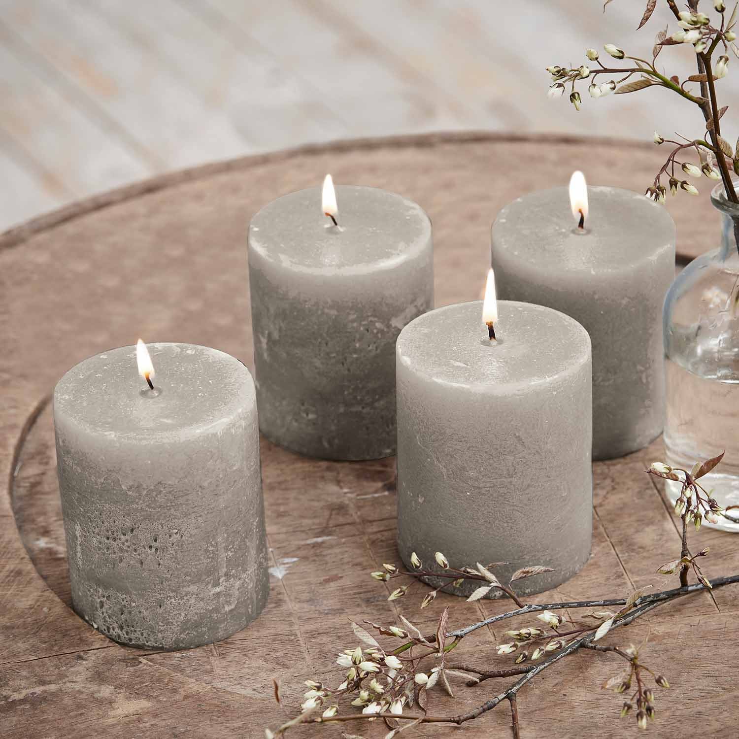 Set di quattro candele cilindriche grigie in cera su tavolo in legno con decorazione floreale