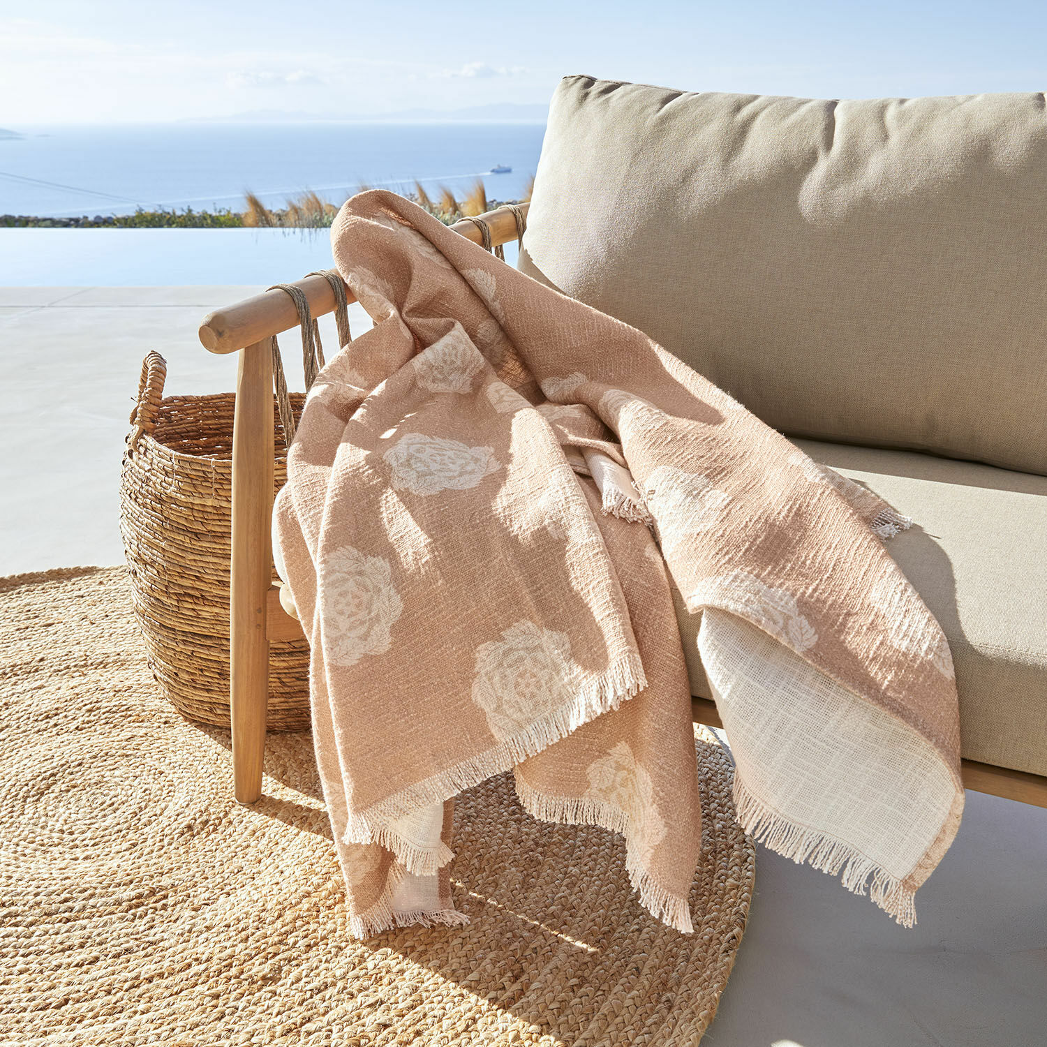 Plaid Belvienne Coperta beige con motivo floreale bianco in tessuto morbido su poltrona in legno su terrazza con vista mare