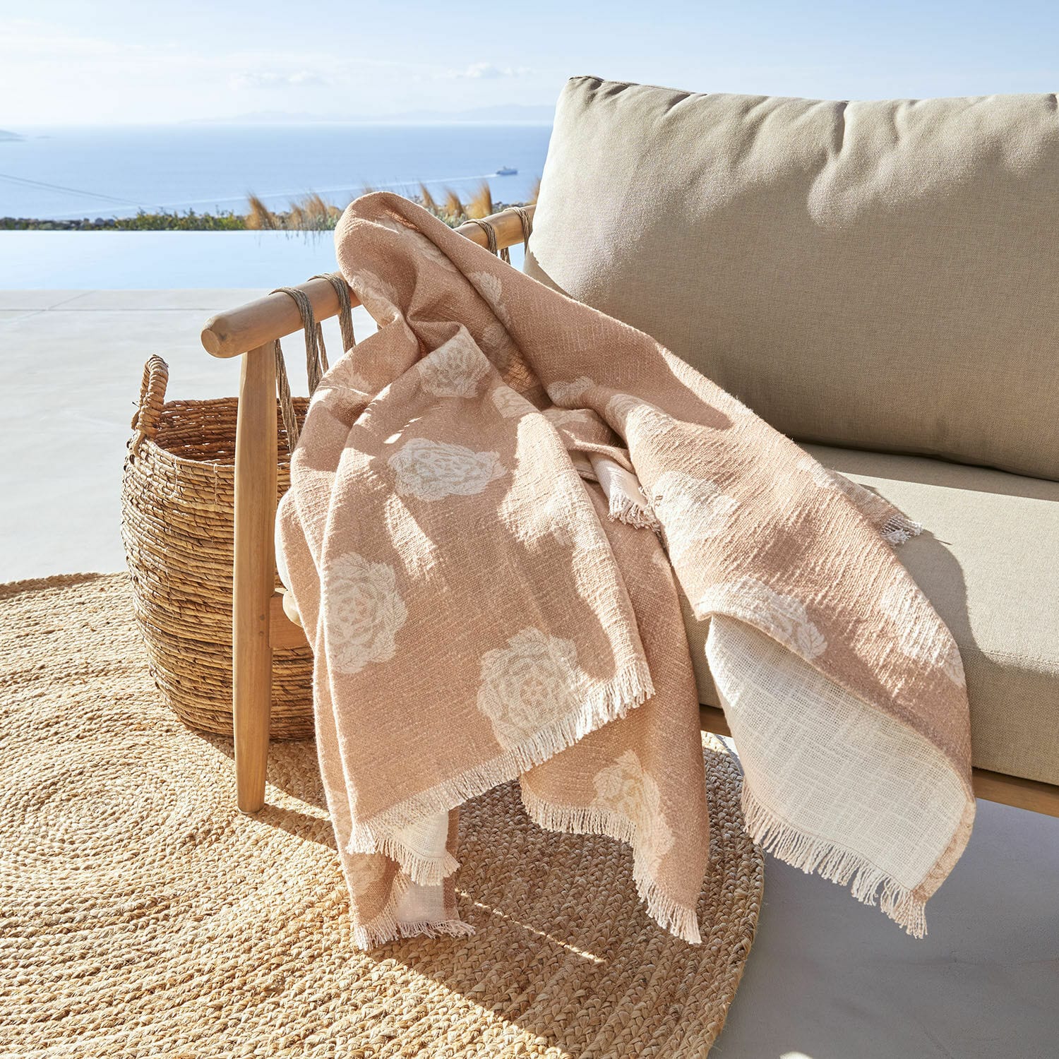 Plaid Belvienne Coperta beige con motivo floreale bianco in tessuto morbido su poltrona in legno su terrazza con vista mare