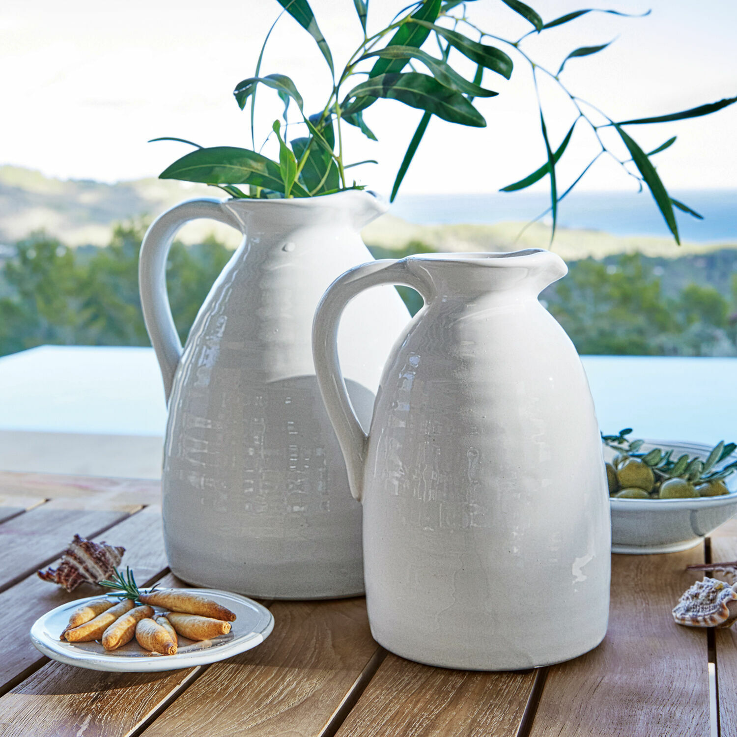 Coppia di vasi Yarick Brocche bianche in ceramica su tavolo in legno con foglie verdi e snack, decorazione tavola