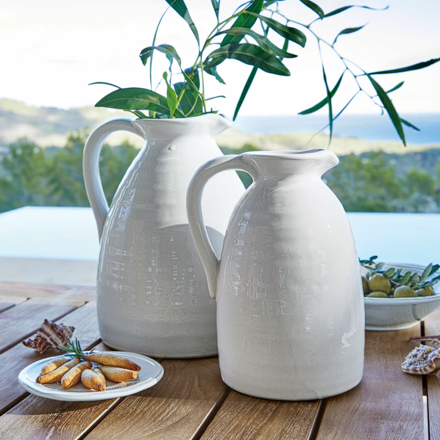 Coppia di vasi Yarick Brocche bianche in ceramica su tavolo in legno con foglie verdi e snack, decorazione tavola